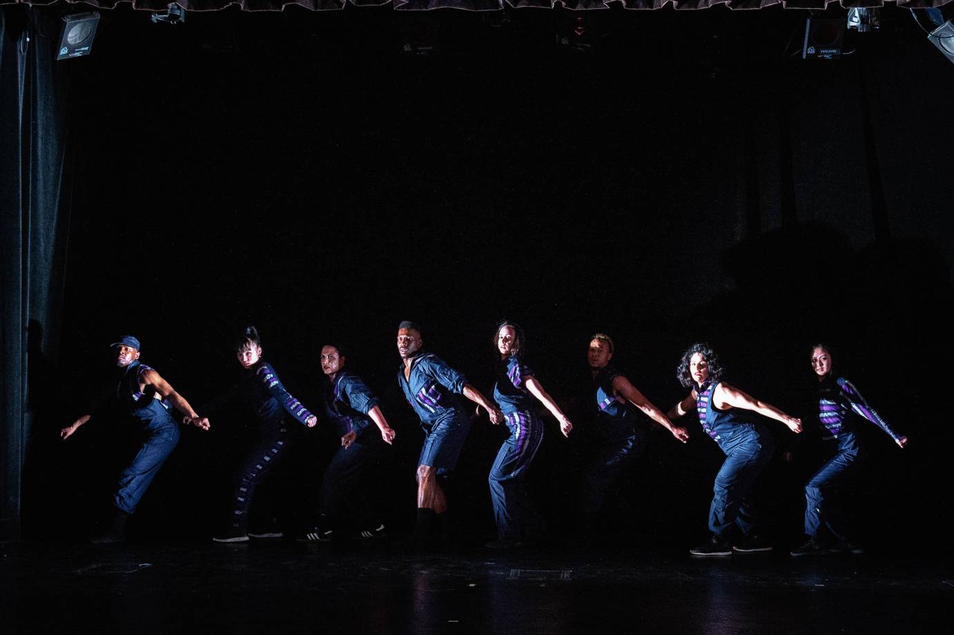 Dancers stand in a line, back arched, knees bent